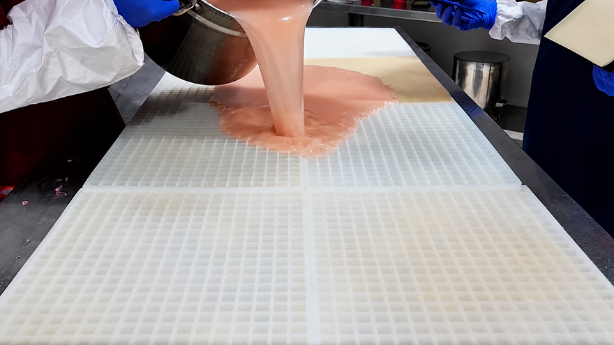 Gummy-Molds-Team gießt Gummimasse über eine große kommerzielle Silikonform vor dem Abstreichen